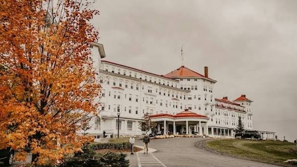 The white, red-roofed Mount Washington Hotel in Bretton Woods, New Hampshire, framed by an autumn maple tree.