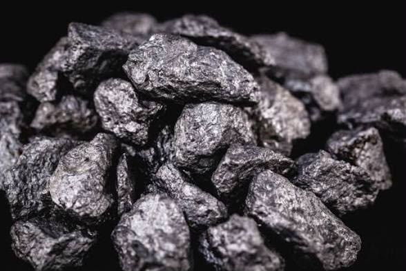 A pile of dark grey rare earth ore concentrate rocks photographed against a black background.