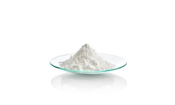 A small pile of fine white refined rare earth oxide powder on a glass watch dish against a white background.